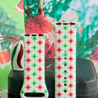Close-up of both Tinsel & Stardust Apple Watch band straps with red and green retro starbursts beside a striped ornament