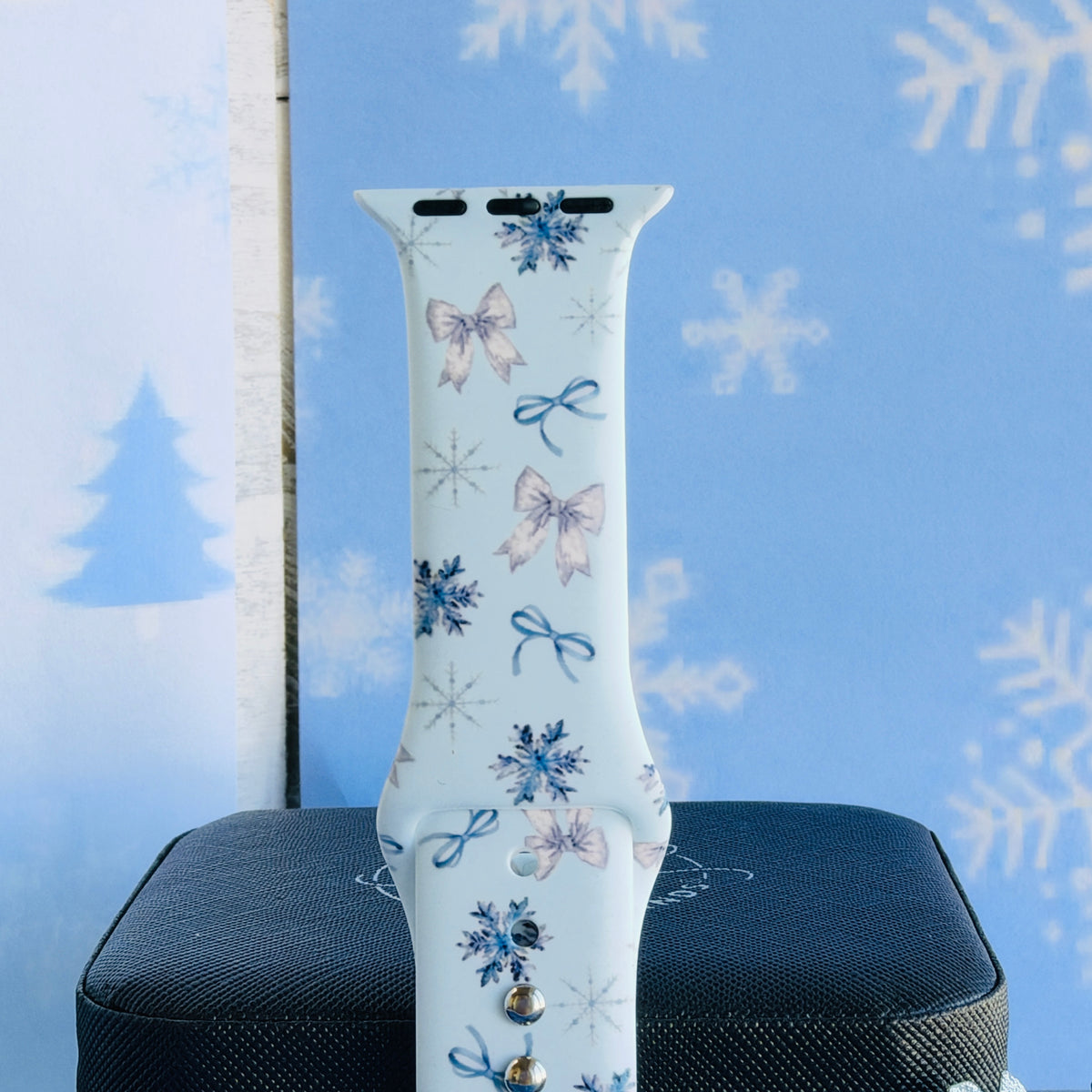 Close-up of a single Snow Pretty In Blue Apple Watch band strap, bow and snowflake print on pale icy blue