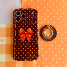 Spotted Looking Cute MagSafe grip ring shown beside the matching Spotted Looking Cute iPhone case with its orange bow, on an orange gingham and polka dot background.