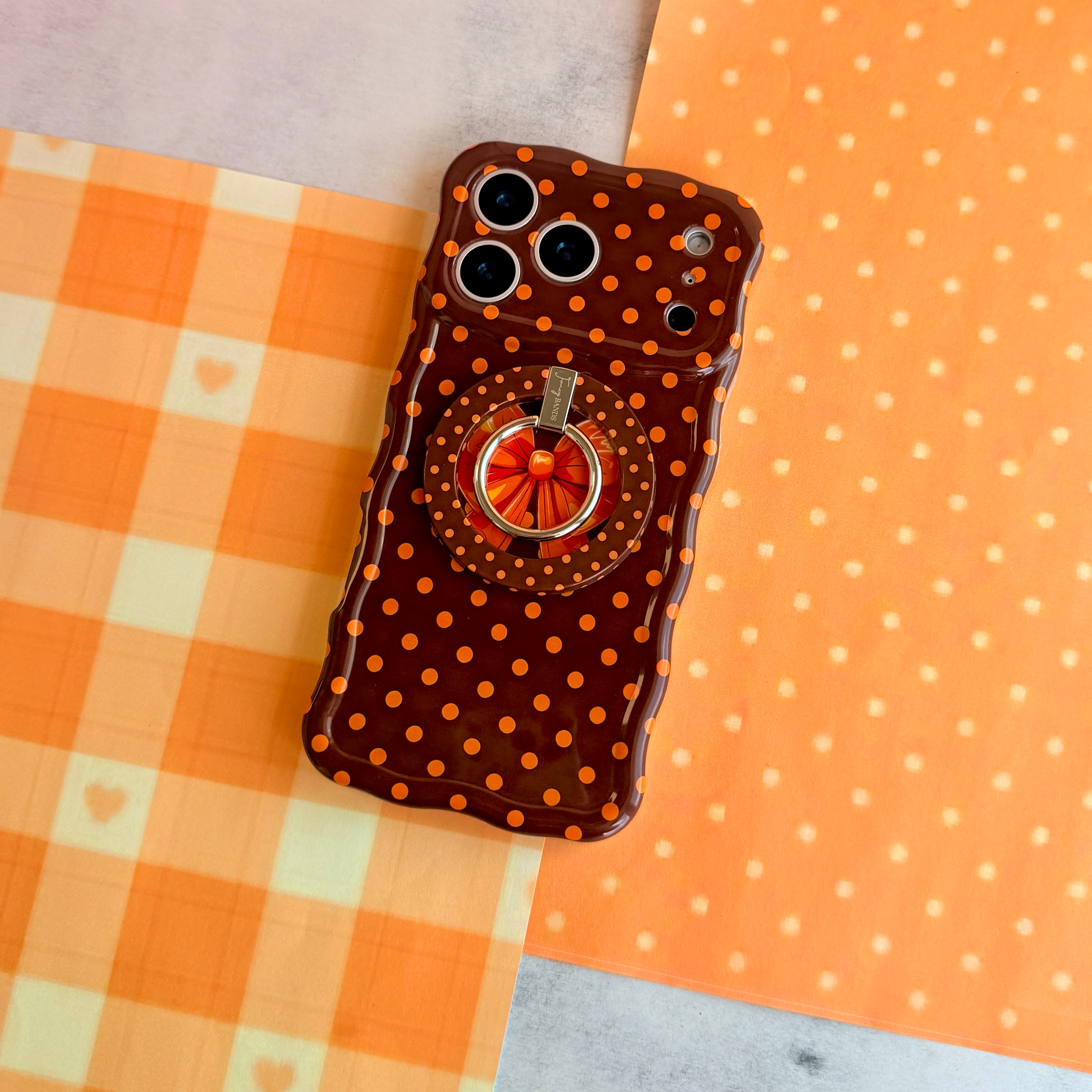Spotted Looking Cute Wavy Luxe iPhone case shown with the matching Spotted Looking Cute MagSafe grip ring attached, styled on orange gingham and polka dot fall decor.