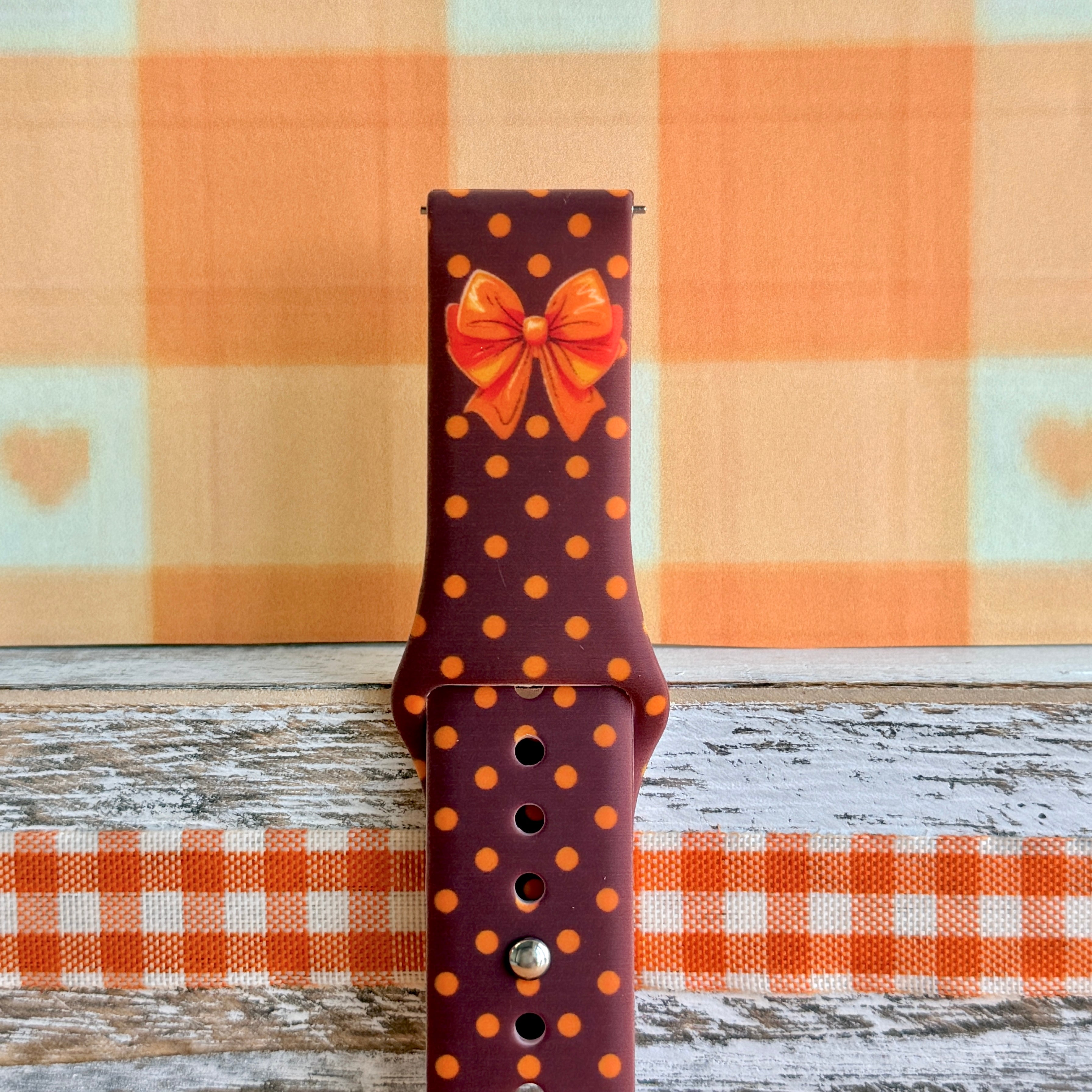 Close-up of the Spotted Looking Cute Samsung Galaxy Watch band showing the orange and red bow artwork and pumpkin-orange dots on chocolate brown silicone.