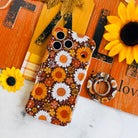 Harvest Sunflowers MagSafe grip ring shown beside the matching Harvest Sunflowers iPhone case, styled against an orange barn wood fall sign with real sunflowers.