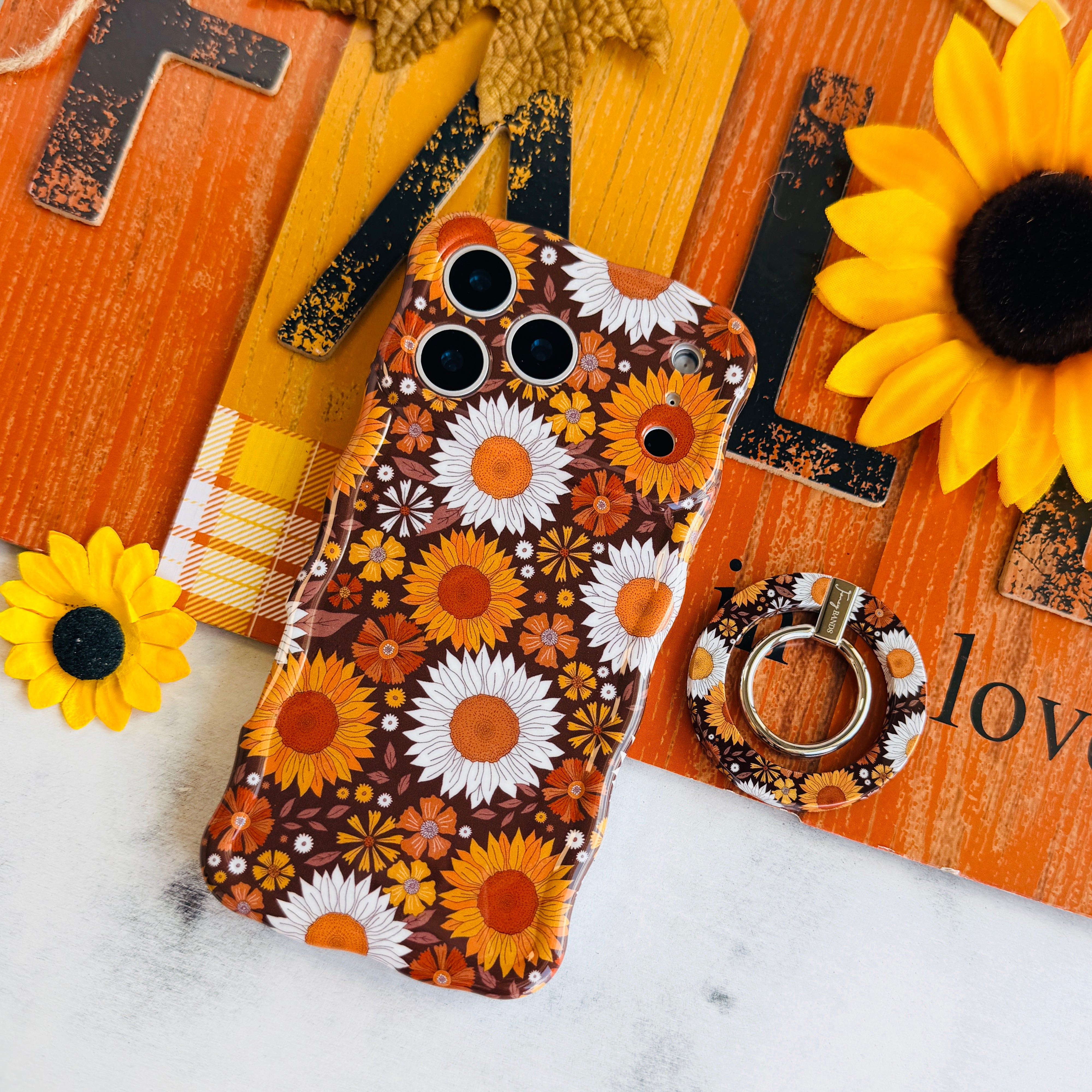 Harvest Sunflowers MagSafe grip ring shown beside the matching Harvest Sunflowers iPhone case, styled against an orange barn wood fall sign with real sunflowers.