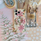 Champagne Snowfall iPhone case with the matching snowflake MagSafe grip ring snapped on, with a gold glitter pom and wooden sleigh