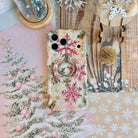 Champagne Snowfall Hold It Fancy MagSafe grip ring snapped onto the matching pink and gold snowflake iPhone case, with a gold glitter pom and wooden sleigh