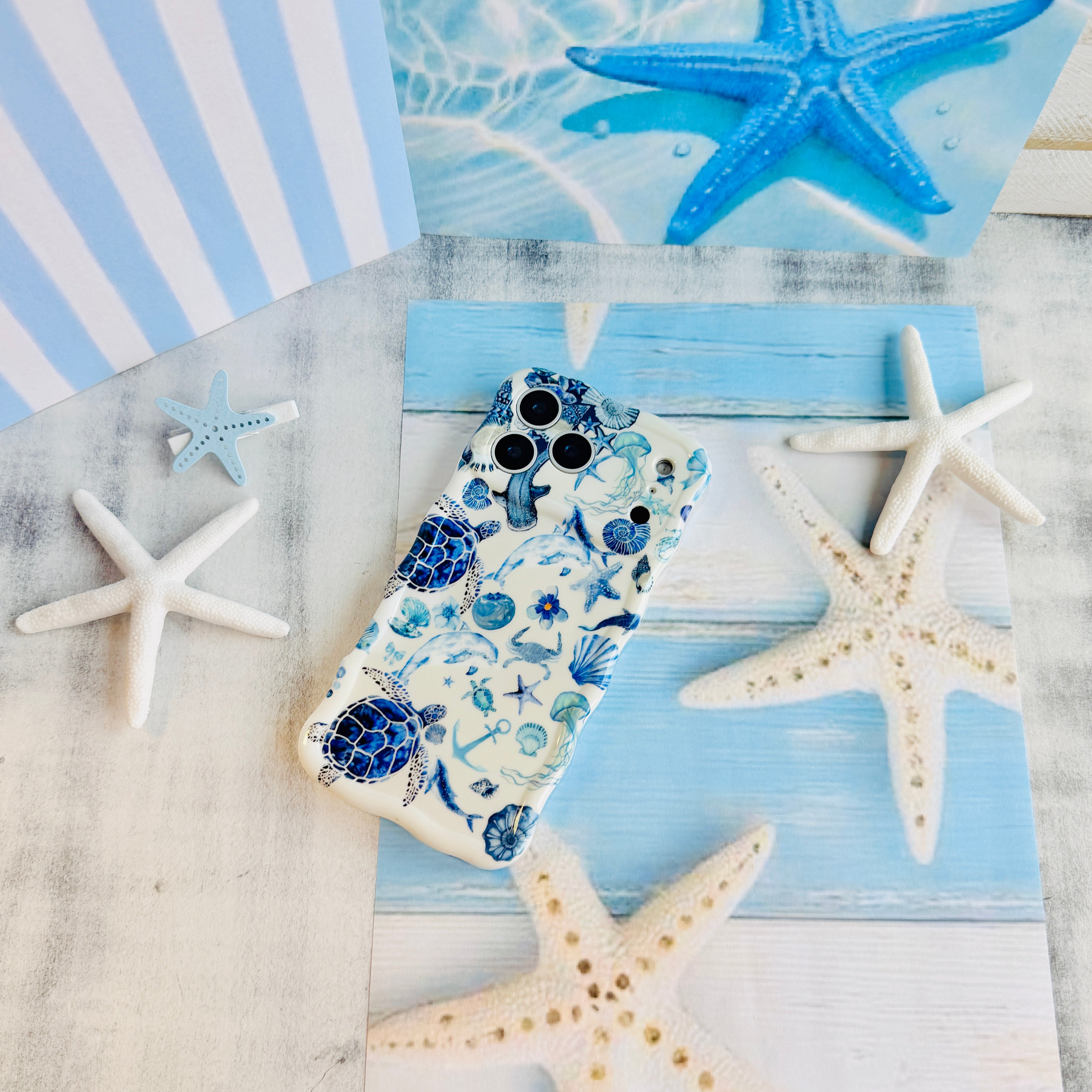Trendy white wavy iPhone case featuring a blue monochrome collage of sea turtles, whales, dolphins, and starfish with a high-gloss finish.