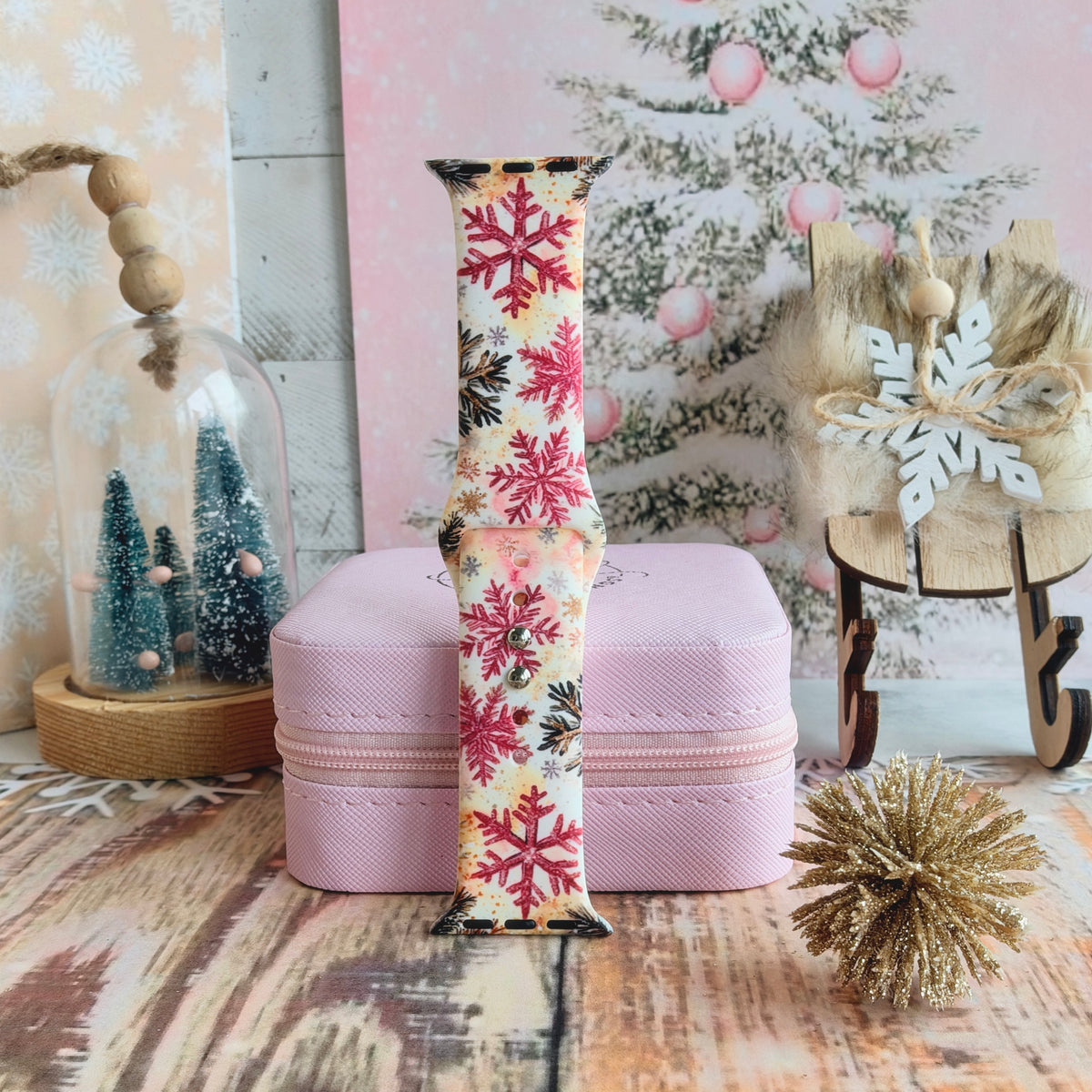 Champagne Snowfall Apple Watch band buckled and standing on a pink jewelry box beside a gold glitter pom and a wooden sleigh