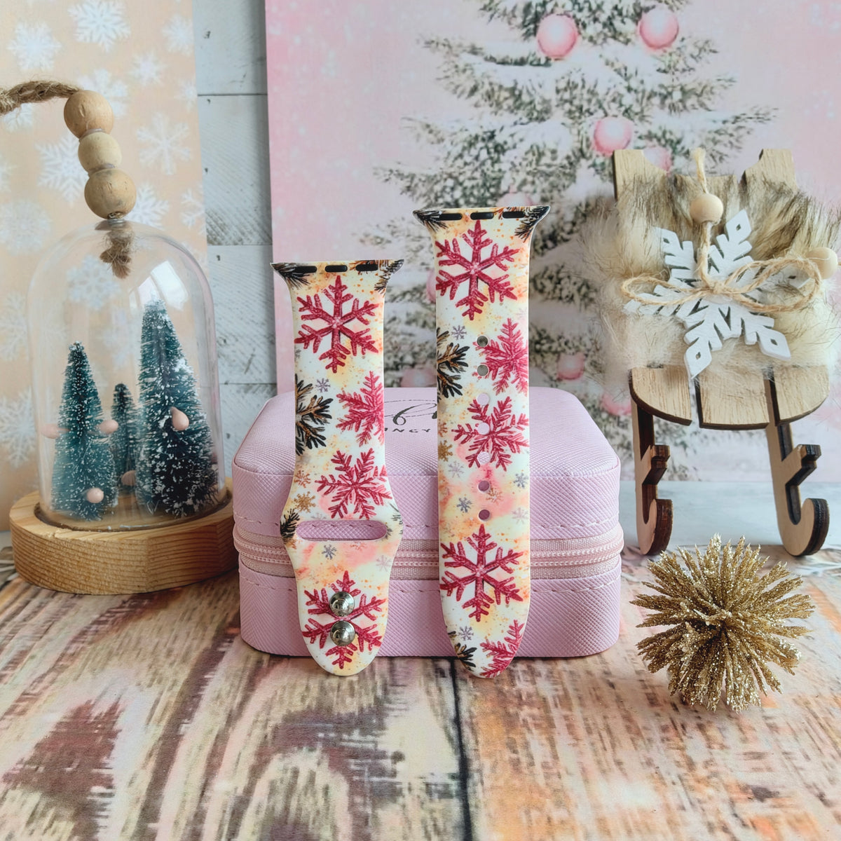 Both Champagne Snowfall Apple Watch band straps on a pink jewelry box with a cloche of bottle-brush trees and a snowy pine backdrop