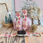 Champagne Snowfall Apple Watch band on a silver Apple Watch and as two straps on a pink jewelry box, pink and gold snowflakes on cream