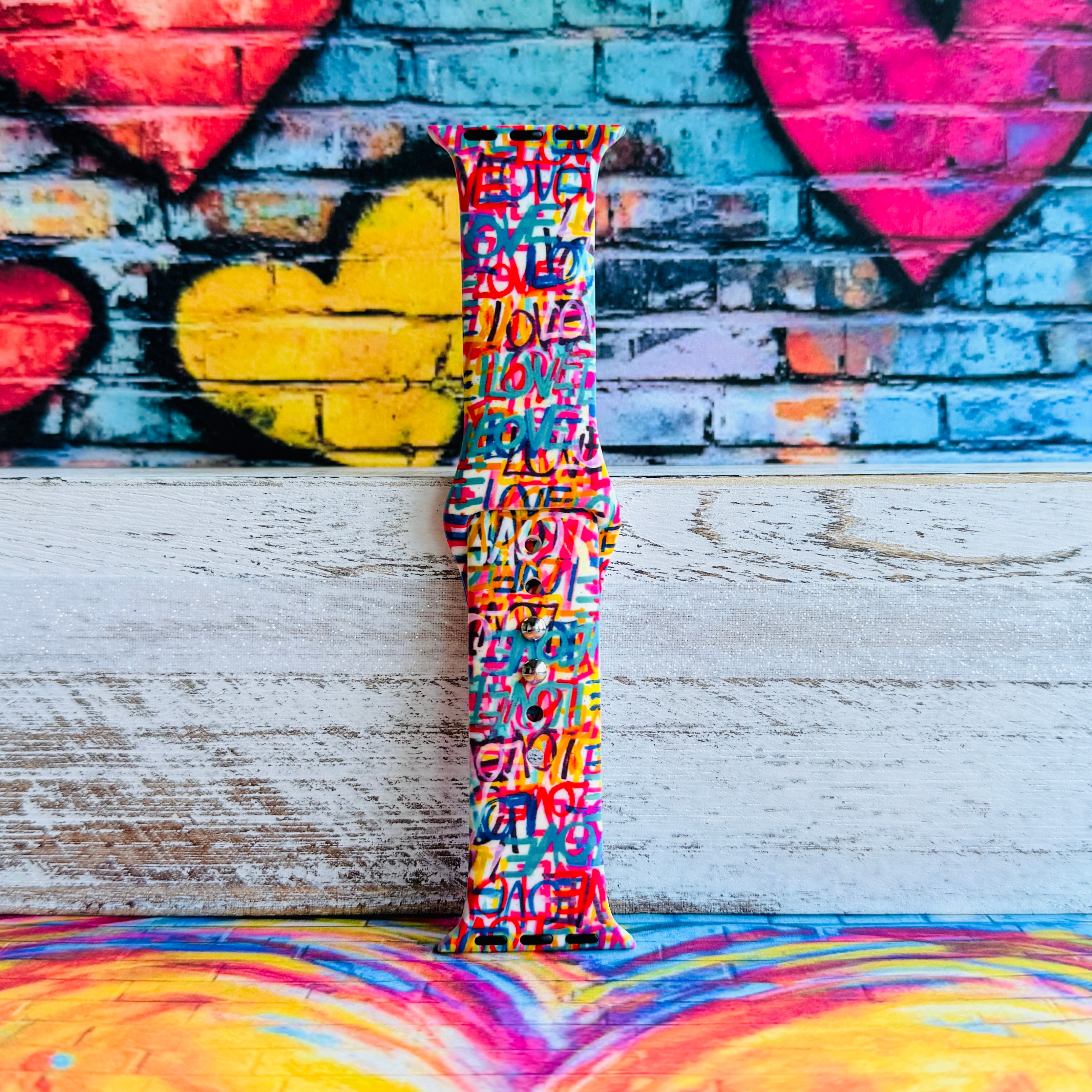 Love Riot Apple Watch band with colorful graffiti "LOVE" text in red, pink, yellow, blue, and turquoise with street art backdrop

