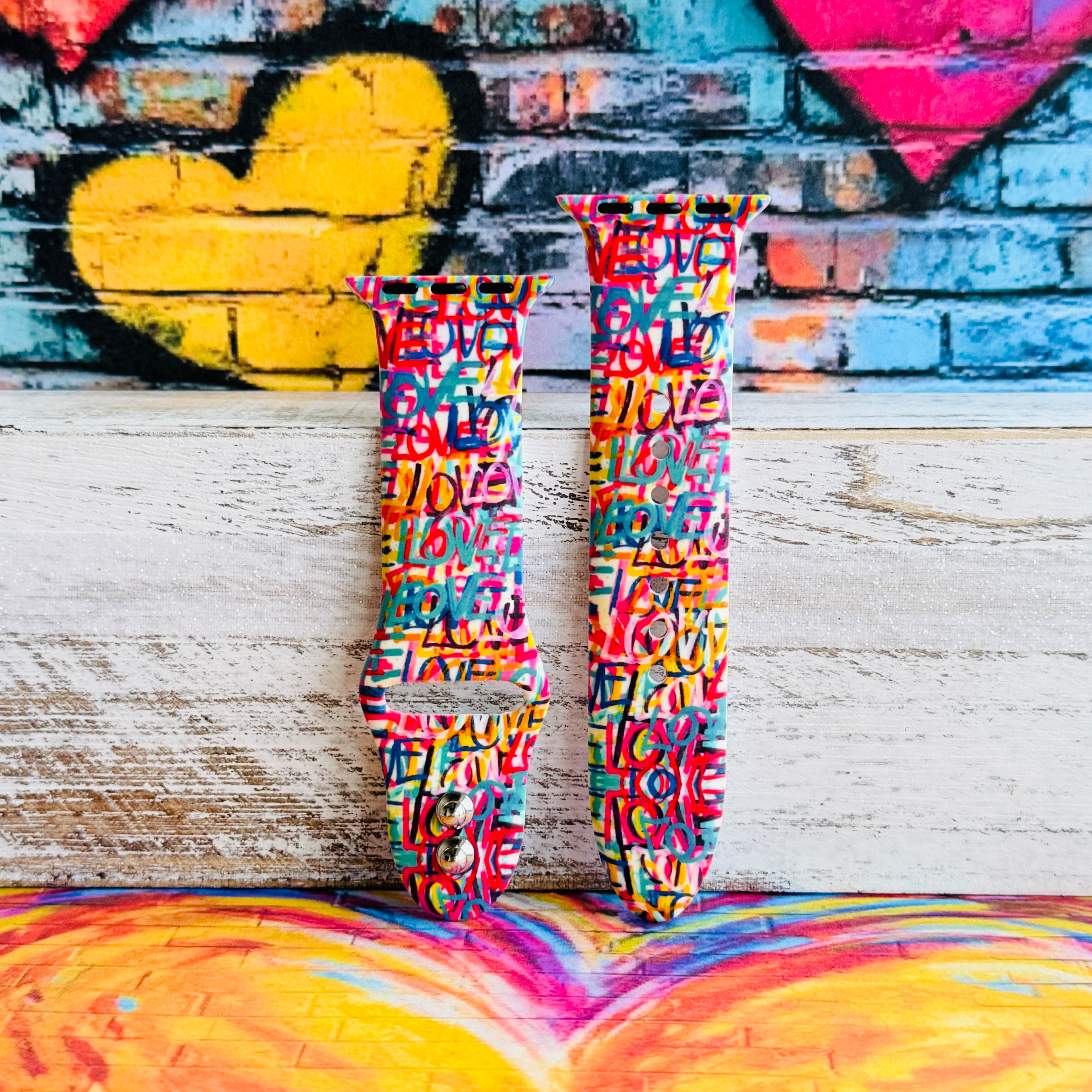 Love Riot Apple Watch band with colorful graffiti "LOVE" text in red, pink, yellow, blue, and turquoise with street art backdrop
