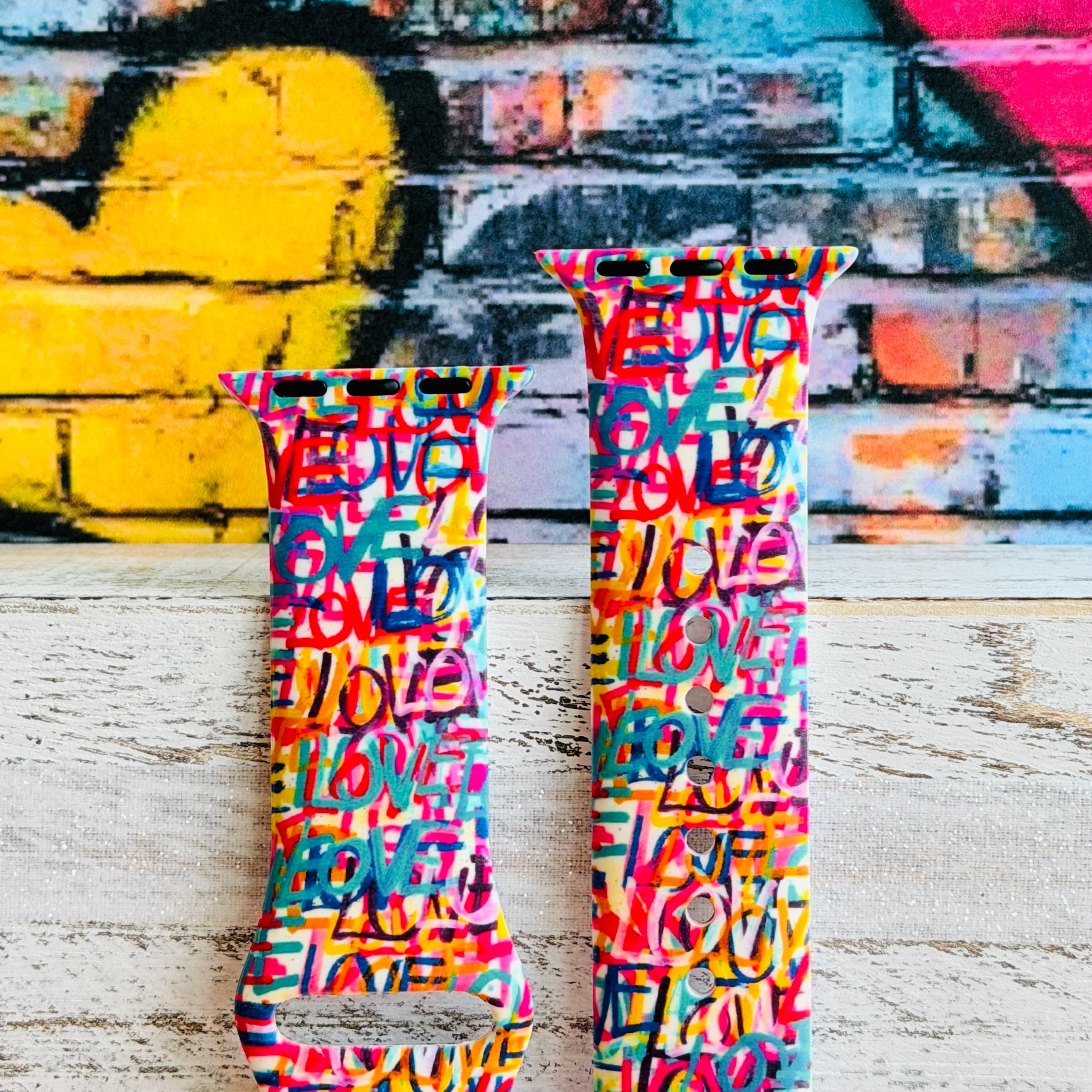 Love Riot Apple Watch band with colorful graffiti "LOVE" text in red, pink, yellow, blue, and turquoise with street art backdrop
