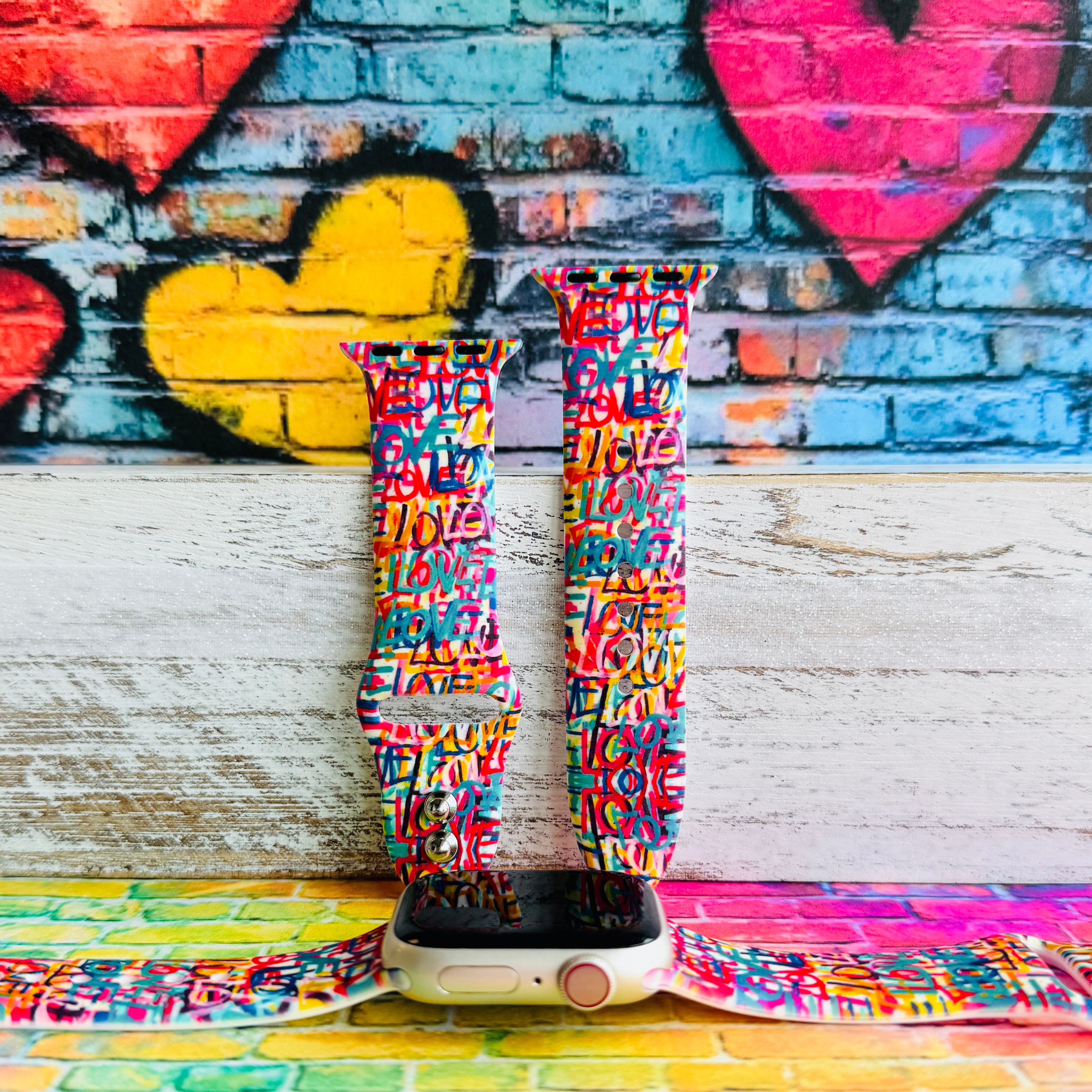 Love Riot Apple Watch band with colorful graffiti "LOVE" text in red, pink, yellow, blue, and turquoise with street art backdrop
