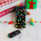 Christmas Lights iPhone case with its black scrunchie wrist strap beside Merry & Bright and happy holidays signs and a green gift