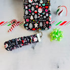 Jolly Wrist-mas scrunchie phone wrist strap clipped below the matching black Christmas iPhone case with a candy cane and green bow