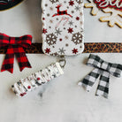 Deer Joy White scrunchie phone wrist strap clipped below the matching reindeer and snowflake iPhone case beside buffalo plaid bows