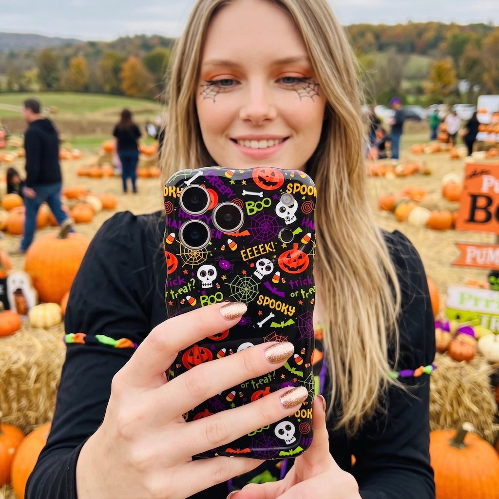 Woman holding the Spooky Wavy Luxe MagSafe iPhone case in a pumpkin patch field, showing the black Halloween print in daylight.