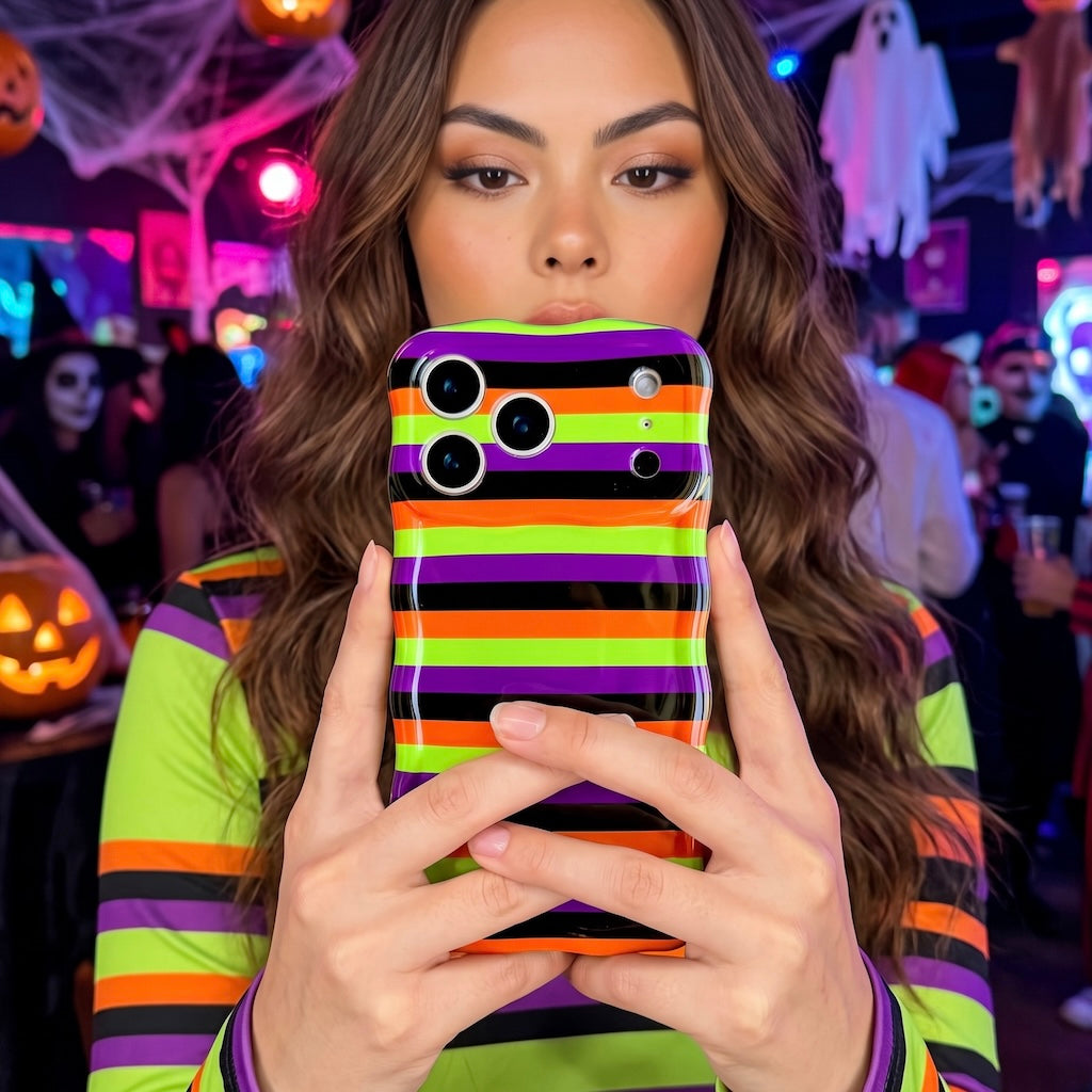 Woman holding the striped Main Witch Energy Wavy Luxe MagSafe iPhone case at a Halloween party lit in orange and purple.