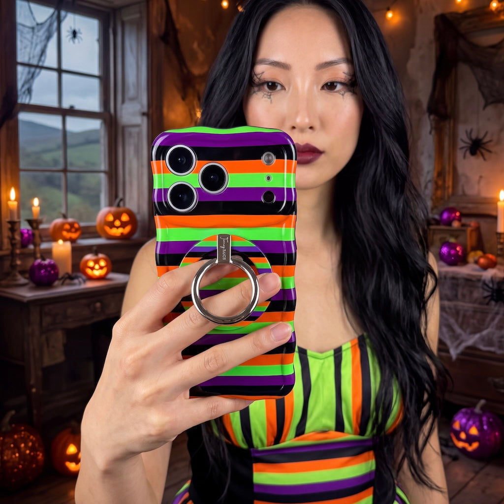 Woman holding the striped Main Witch Energy Wavy Luxe MagSafe iPhone case with the matching grip ring attached, indoors by candlelight.