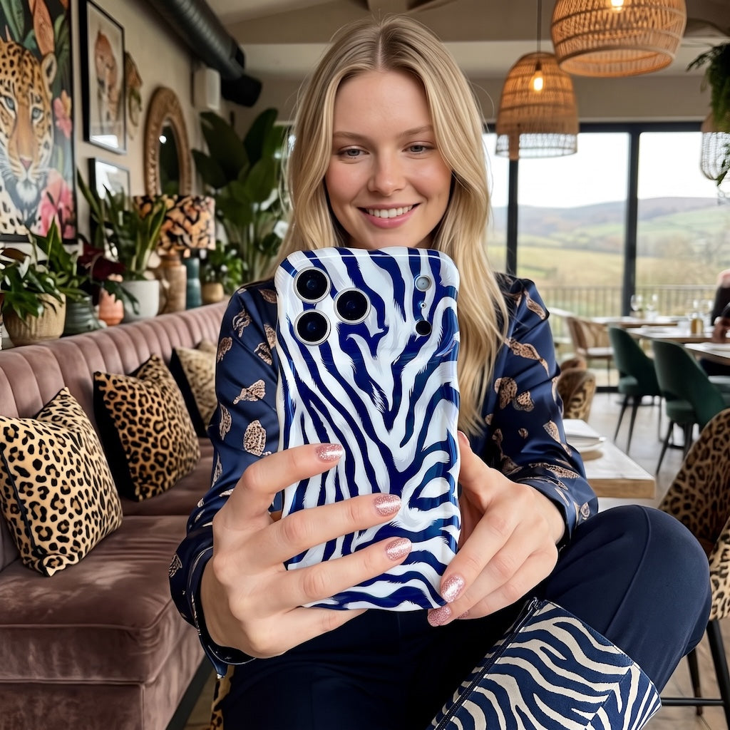 Woman taking a selfie with the Zebra, Obviously navy zebra print iPhone case in a lounge with leopard cushions and a velvet sofa, wearing matching zebra print jeans.