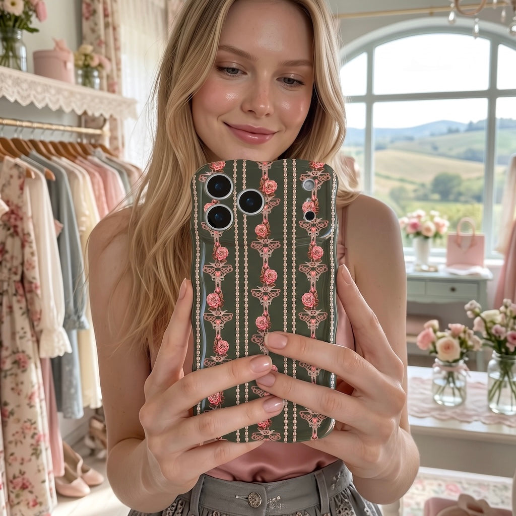 Woman in a pink top holding up the Pretty Little Details black pearl and rose iPhone case in a floral boutique with arched windows.