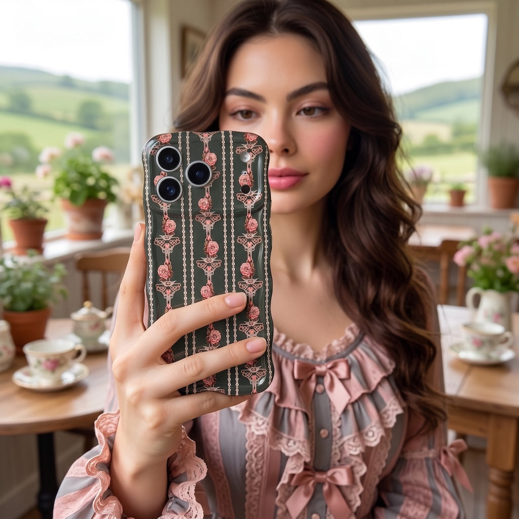 Woman in a ruffled pink blouse taking a mirror selfie with the Pretty Little Details black pearl and rose iPhone case in a cottage kitchen with a tea set.