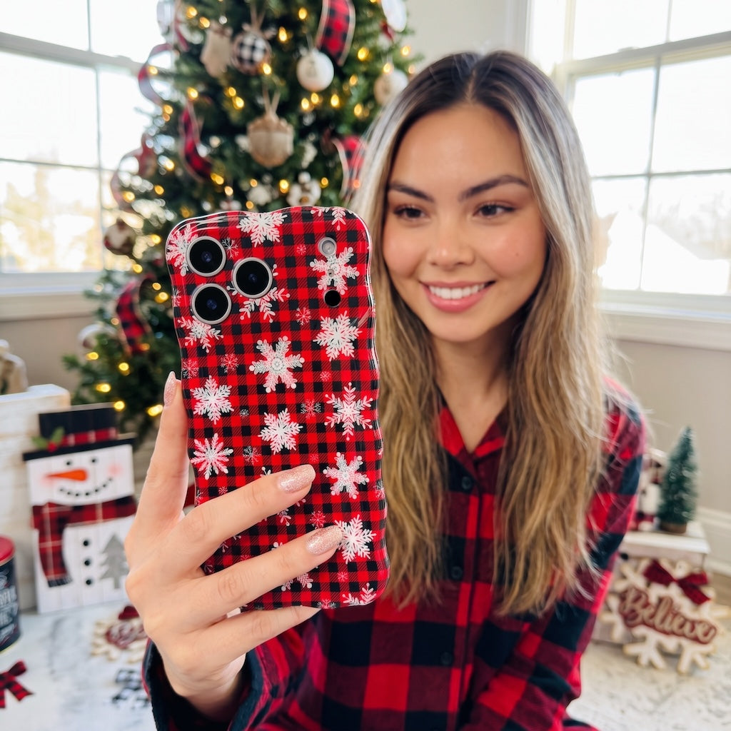Smiling woman in a red flannel shirt taking a selfie with her Buffalo Plaid Snowflake iPhone case next to a Christmas tree