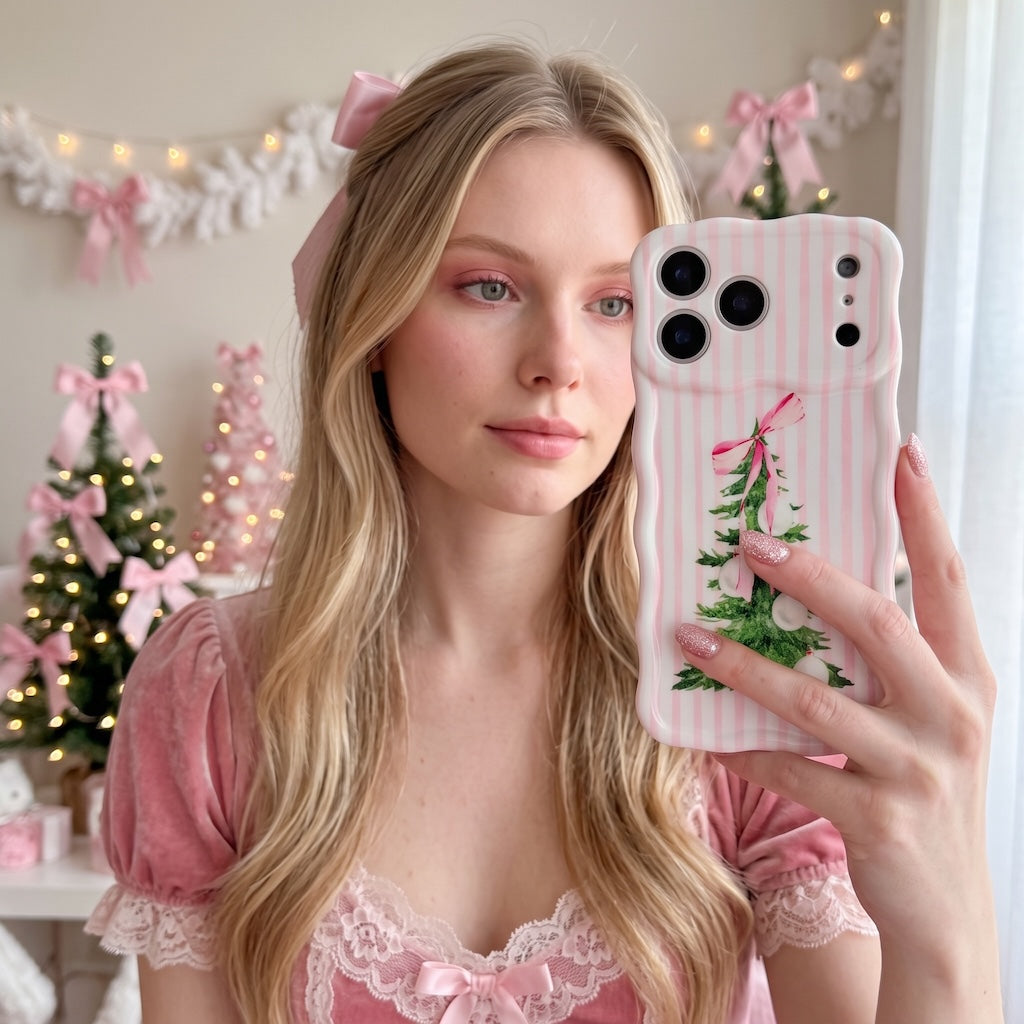Blonde woman in a pink velvet dress holding her Pretty in PinkMas iPhone case in front of pink bows and a Christmas tree