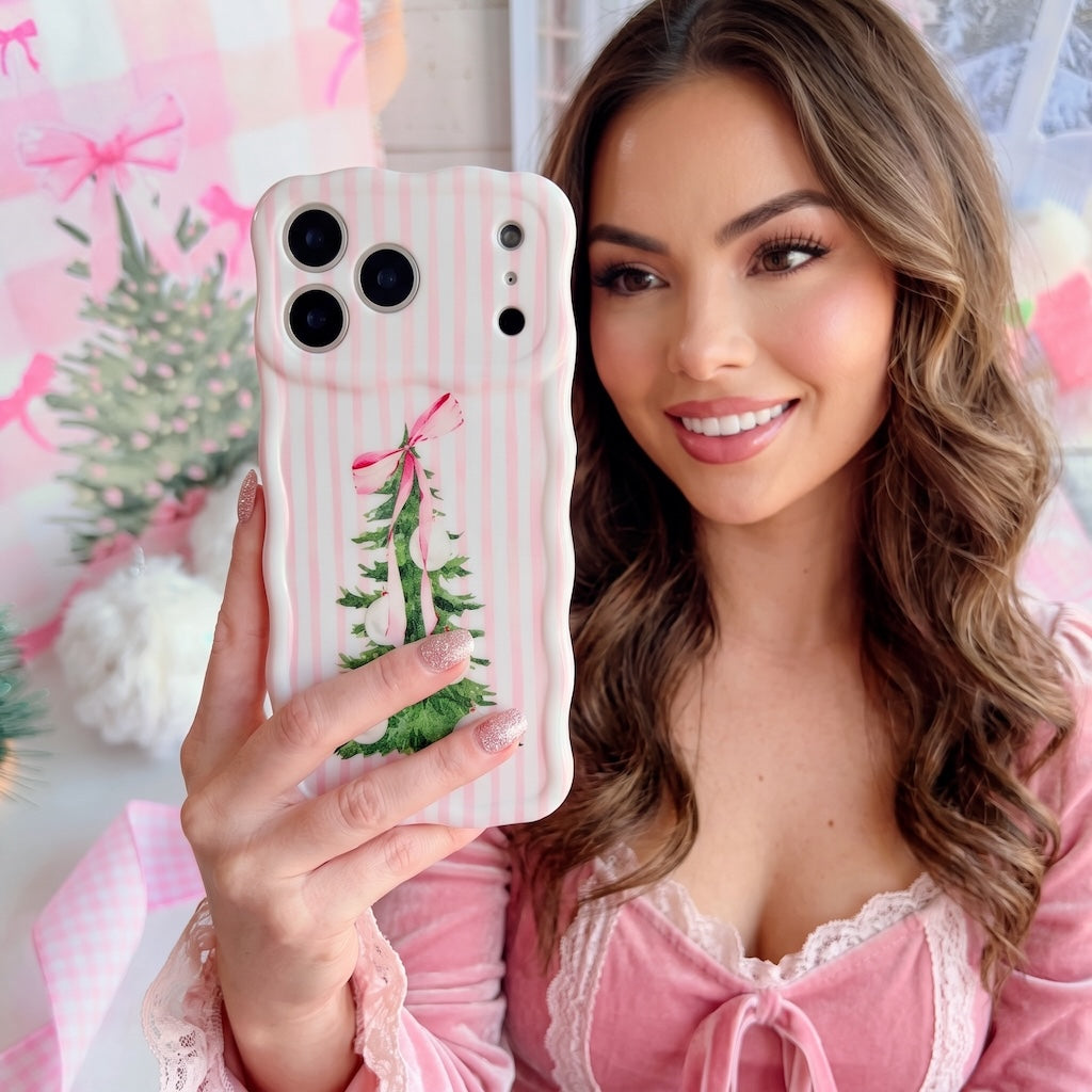 Woman with long brown hair in a pink velvet and lace dress taking a selfie with her Pretty in PinkMas iPhone case in a pink Christmas room