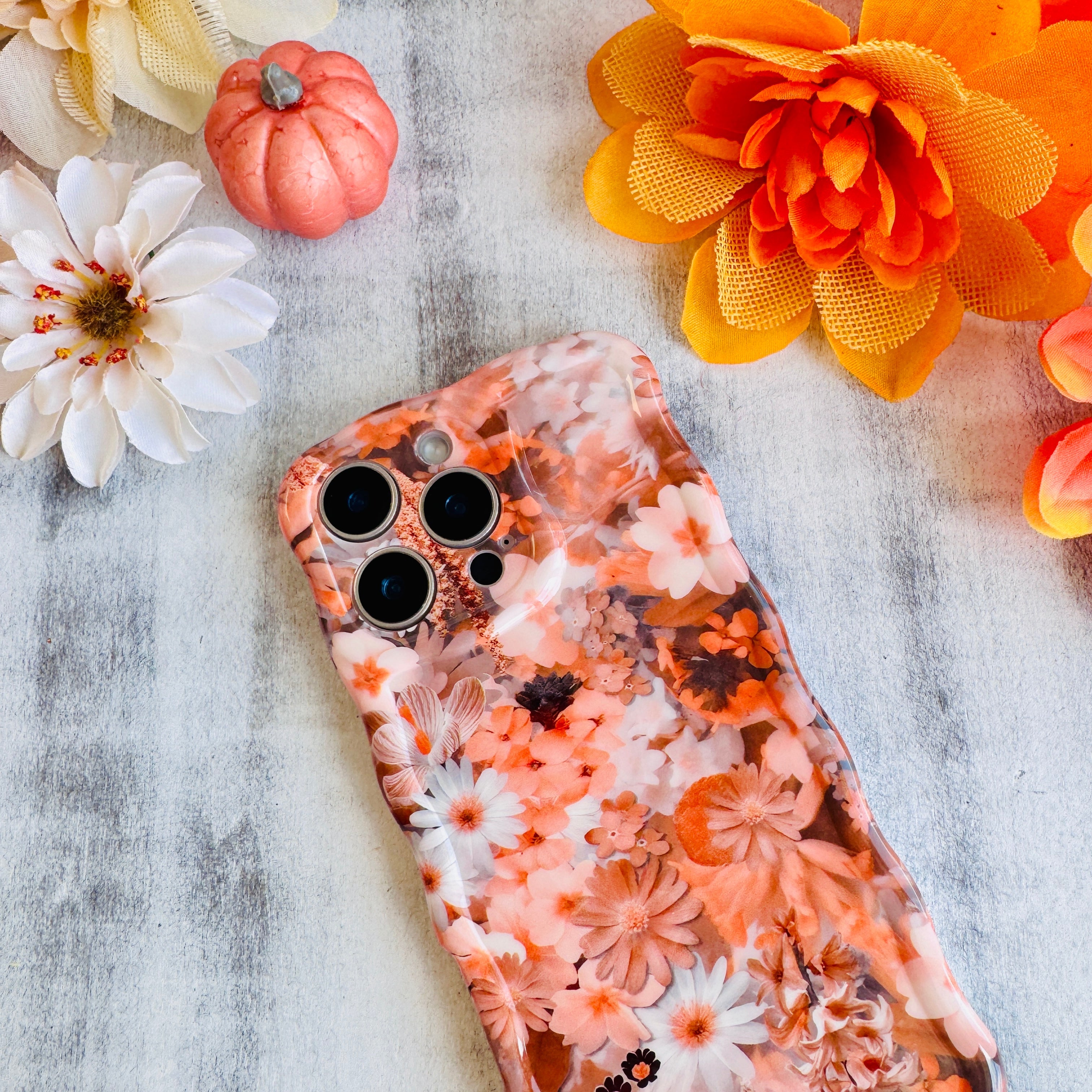 Fall Blooms Wavy Luxe MagSafe iPhone case with a warm autumn floral print in orange and cream, styled with fall decor