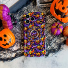 Jack-O-Lantern Jive Hold It Fancy MagSafe grip ring attached to the matching Wavy Luxe iPhone case, styled with orange pails and magenta glitter pumpkins