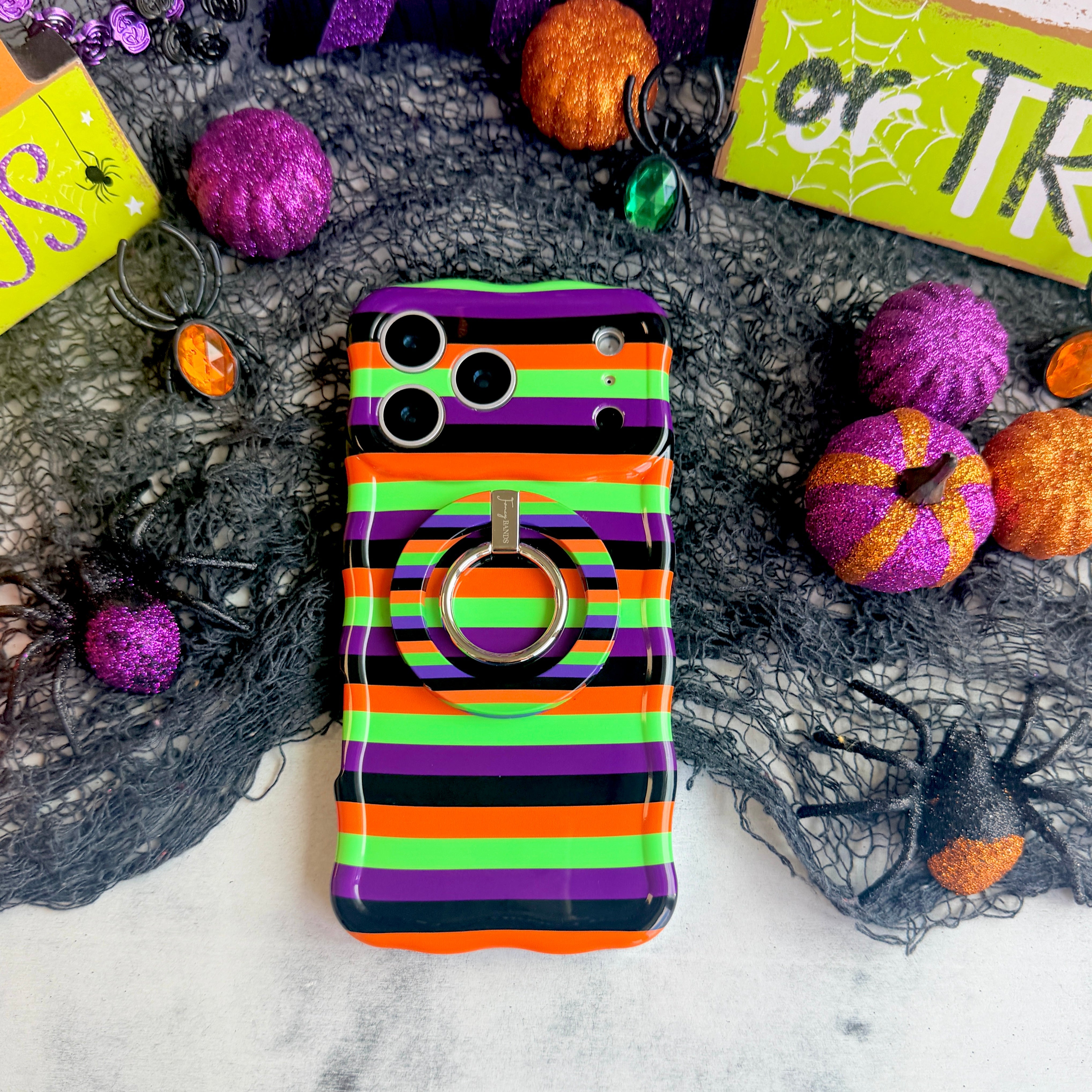 Main Witch Energy Hold It Fancy MagSafe grip ring attached to the matching striped iPhone case, styled with glitter pumpkins and a spider