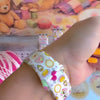 It's Giving Grandma Hobbies silicone Apple Watch band with "hot girls have grandma hobbies" script, patchwork hearts, yarn balls, knitting needles, embroidery hoops, lanterns, pies, and teacups on a cream base, shown displayed and worn on Apple Watch against a cottagecore craft backdrop.