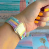 Sweet Summer silicone Apple Watch band with pastel pink, yellow, and blue surfboards, palm trees, and "sweet summer time" script on a soft watercolor beach scene, shown displayed and worn on Apple Watch against a coastal surfboard backdrop.
