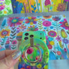 Petal Princess watercolor floral MagSafe phone grip ring with vibrant pink and yellow blooms on green background compatible with iPhone and Samsung
