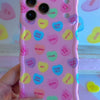 Pink wavy iPhone case featuring colorful candy conversation hearts with text like Be Mine, Ur Hot, and Soul Mate.