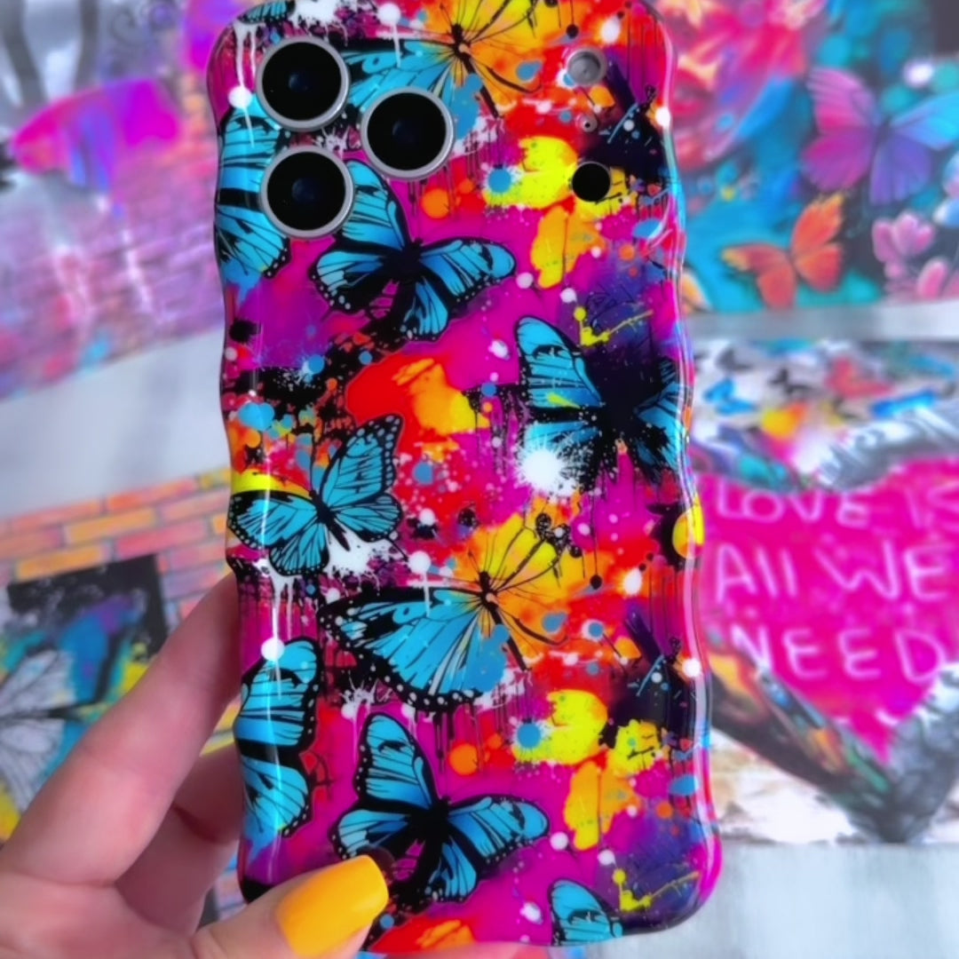 Trendy wavy iPhone case featuring a vibrant street-art collage of electric blue and yellow butterflies over neon pink paint splatters with a high-gloss finish.