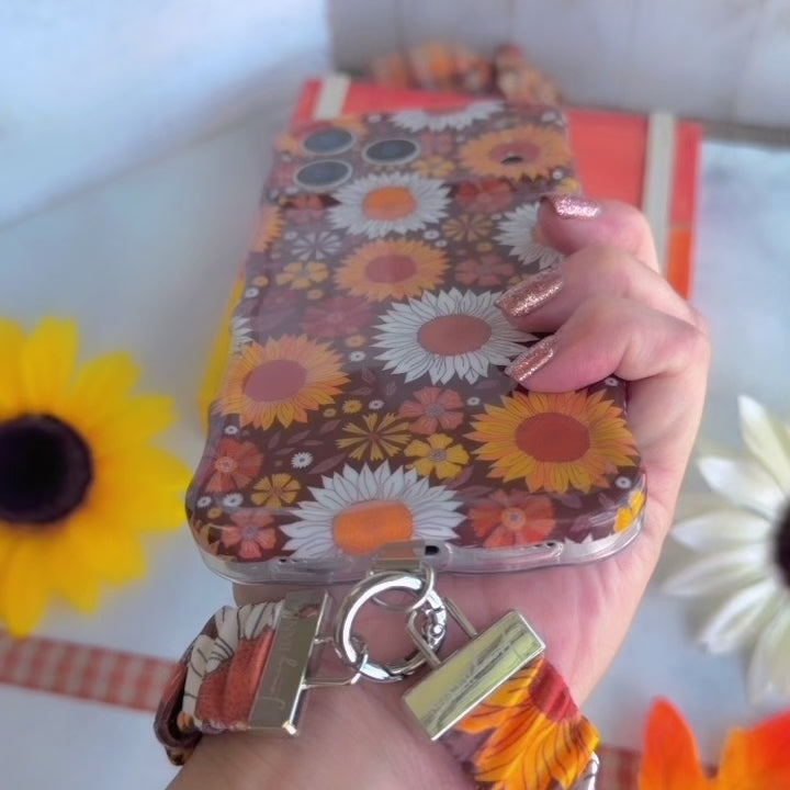 Video of the Harvest Sunflowers scrunchie phone wrist strap showing the deep brown fabric packed with golden sunflowers and white daisies, the silver clasp, and how it attaches to a phone case.