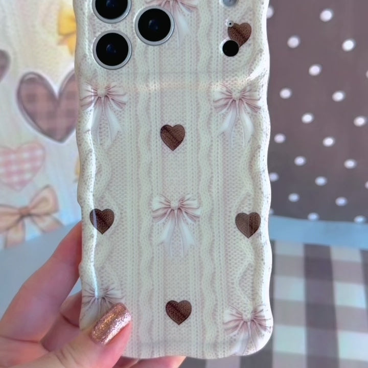 Video showing the Sweater Weather Sweetheart Wavy Luxe MagSafe iPhone case from multiple angles, featuring the cream cable-knit print with taupe bows and brown hearts.