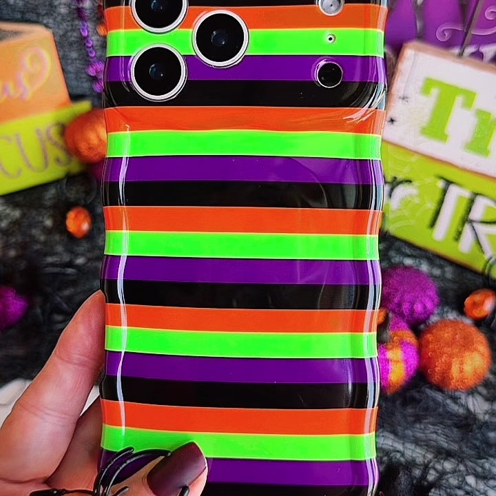 Video of the Main Witch Energy Wavy Luxe MagSafe iPhone case turning in hand to show the black, purple, green and orange stripes and the wavy edge.