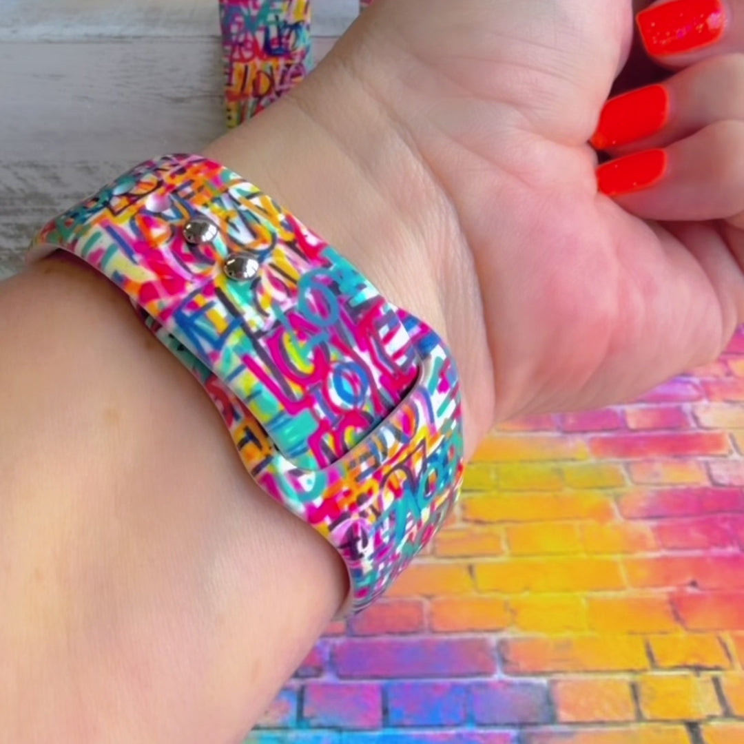 Love Riot Apple Watch band with colorful graffiti "LOVE" text in red, pink, yellow, blue, and turquoise with street art backdrop
