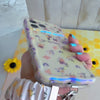 A sweet Bee Happy scrunchie phone wrist strap in a white bumblebee, honeycomb, and honey-pot print, clipped to the matching Bee Happy Wavy Luxe iPhone case, styled with sunflowers and bees on a soft cream background.