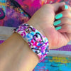 Love Out Loud silicone Apple Watch band with hand-drawn graffiti-style hearts in pink, magenta, blue, teal, red, and black on a white base, shown displayed and worn on Apple Watch against a colorful street art backdrop.