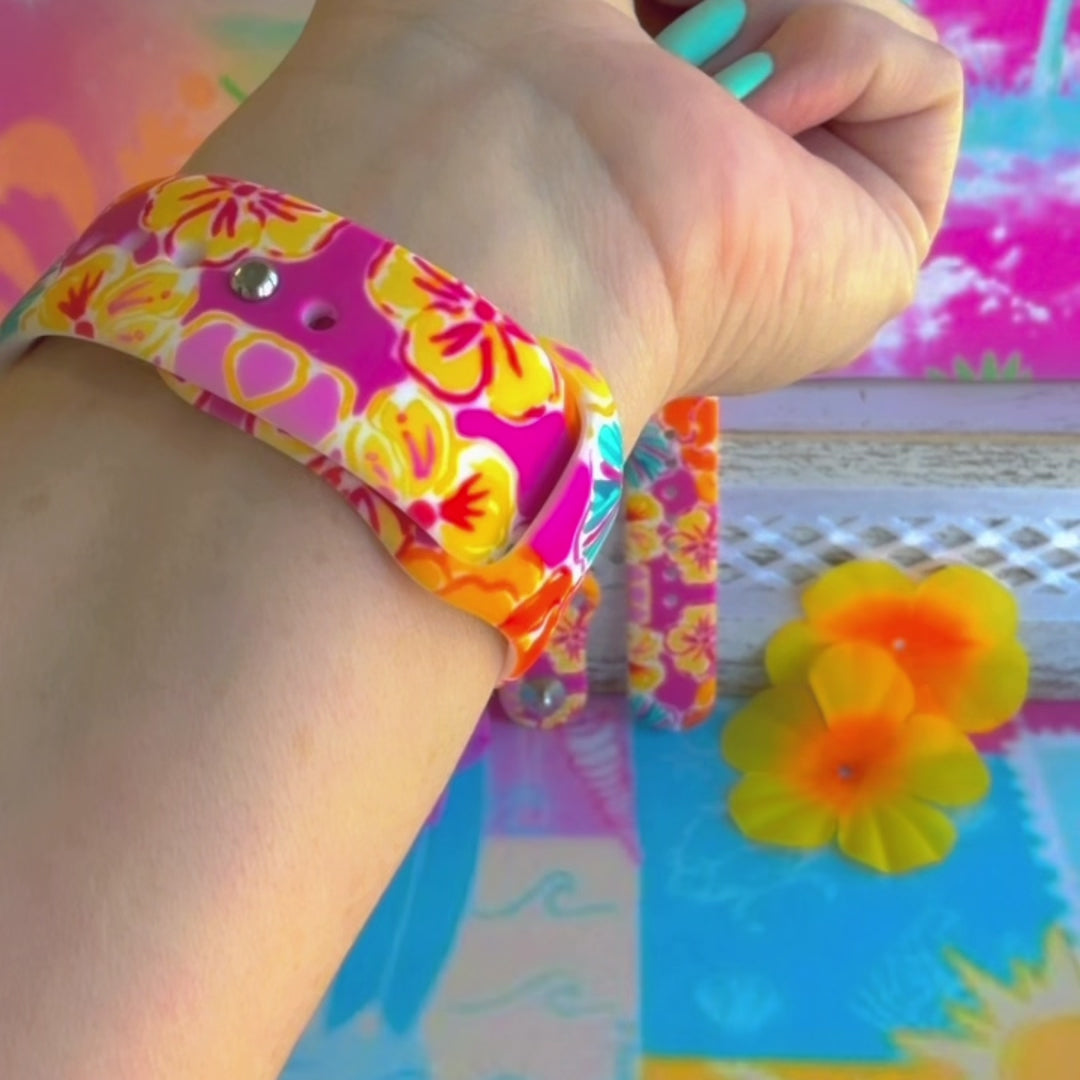 Sunset Hibiscus silicone Samsung Watch band with vibrant pink, orange, yellow, and teal tropical hibiscus floral print, shown displayed and worn on Apple Watch against a colorful tropical floral backdrop.