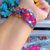 Rebel Wings silicone Samsung Galaxy Watch band with graffiti-style butterflies in blue, orange, yellow, and white over a hot pink and magenta paint-splatter background, shown displayed and worn against a colorful street art butterfly backdrop.