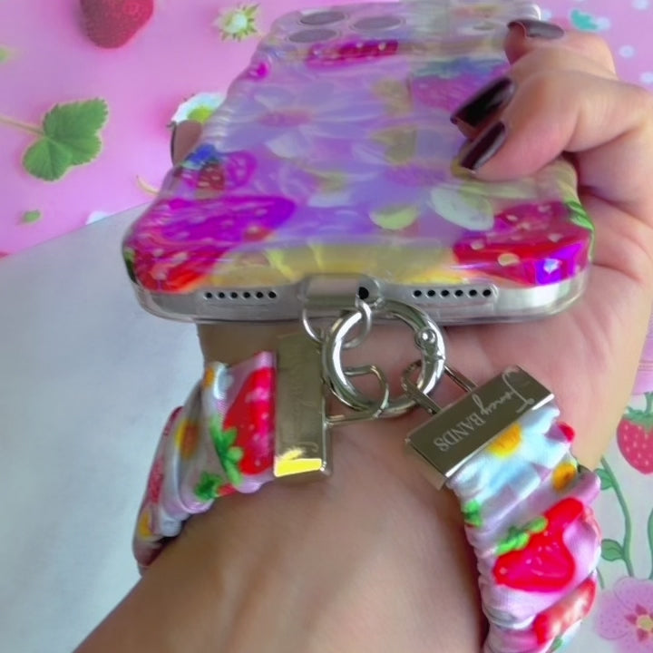 Video of the Berry Cute Blooms Scrunchie Phone Wrist Strap worn on the wrist and clipped to the matching case, showing the gathered pink strawberry and daisy fabric and silver clasp.