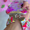 Video of the Berry Cute Blooms Scrunchie Phone Wrist Strap worn on the wrist and clipped to the matching case, showing the gathered pink strawberry and daisy fabric and silver clasp.