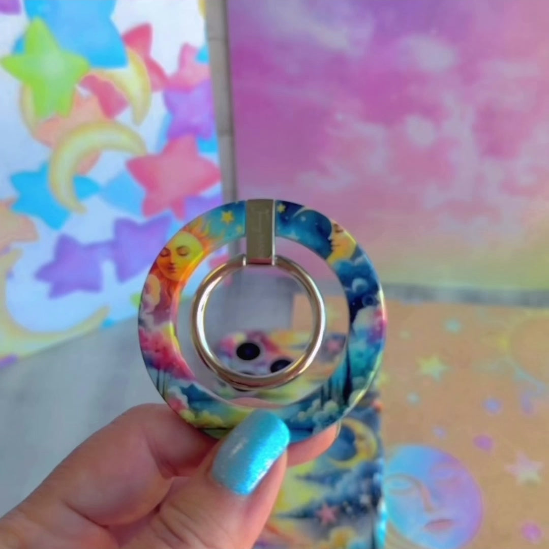 Cosmic Daydream celestial MagSafe phone grip ring with watercolor illustration of a personified sun, crescent moon, and stars in a dreamlike landscape compatible with iPhone and Samsung