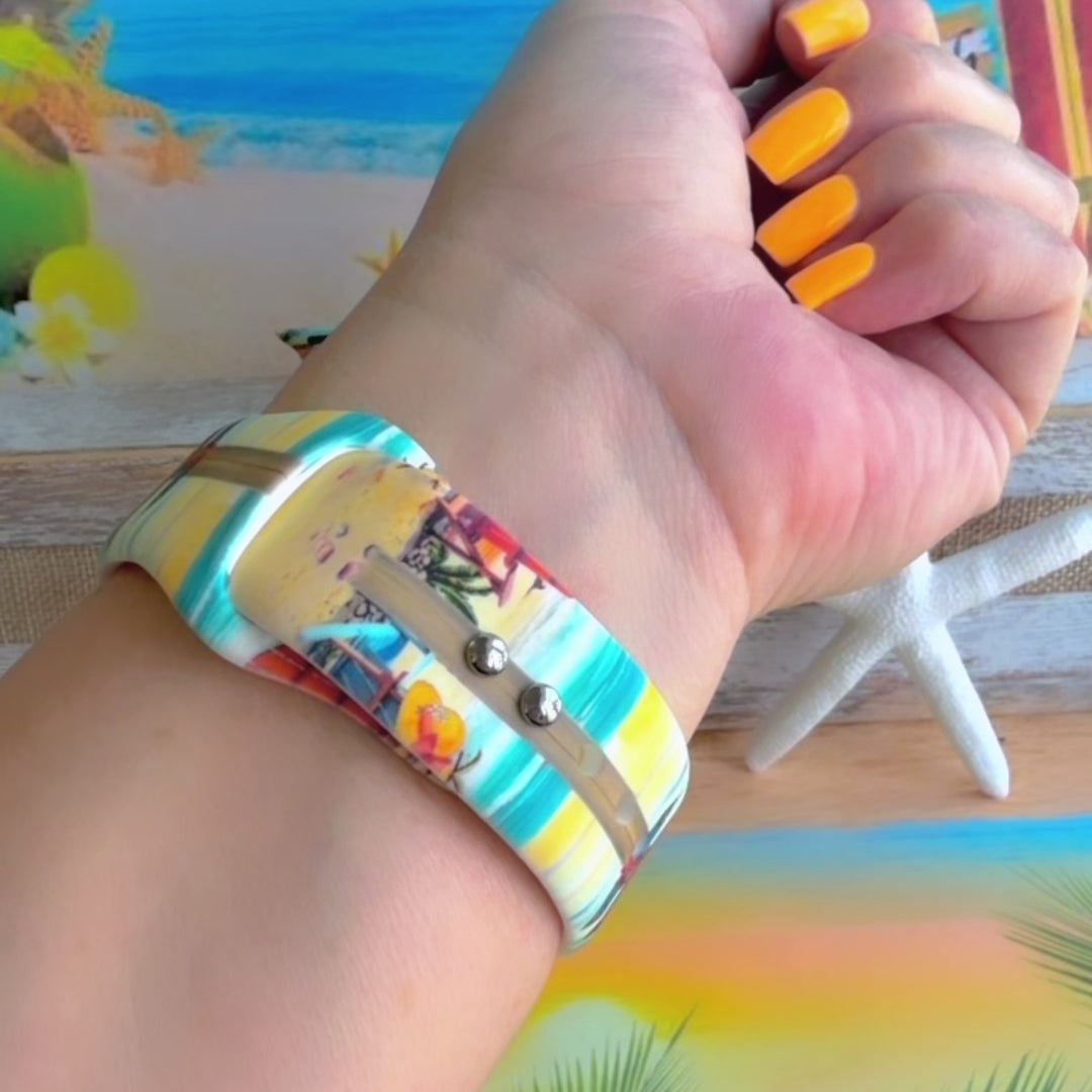 Seaside State of Mind silicone Apple Watch band with colorful surfboard signpost on a beach scene and "Be Crazy, Be Silly, Be Weird—life is too short to be anything but happy" message, shown displayed and worn on Apple Watch against a beach backdrop.