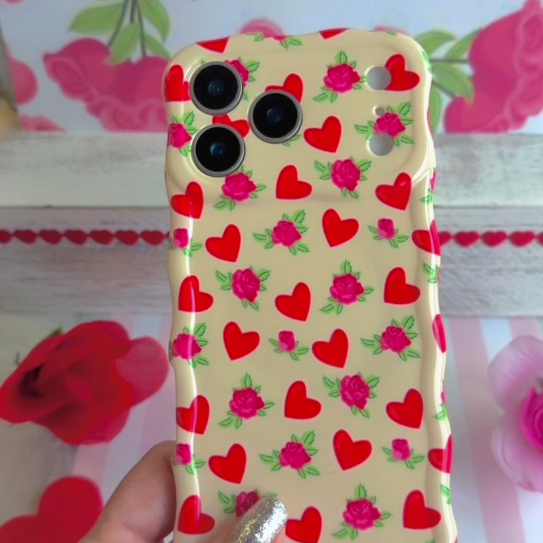 Cream colored wavy iPhone case featuring a pattern of red hearts and small pink roses with green leaves.